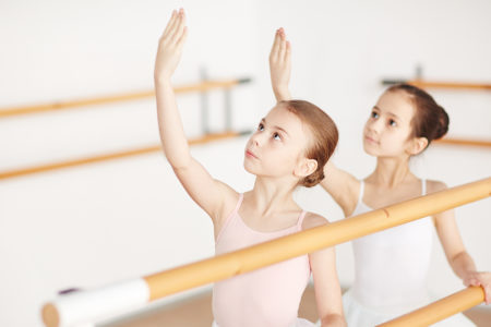 Small group of little girls in ballet dresses looking at their raised hands